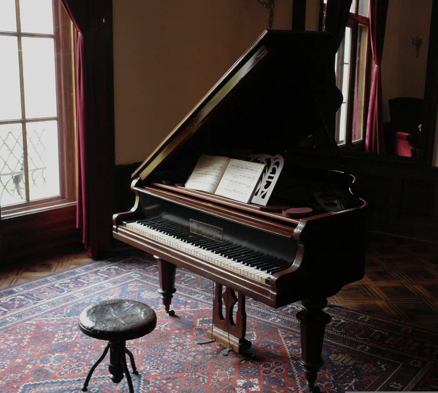 An antique grand piano by a window in a quiet room